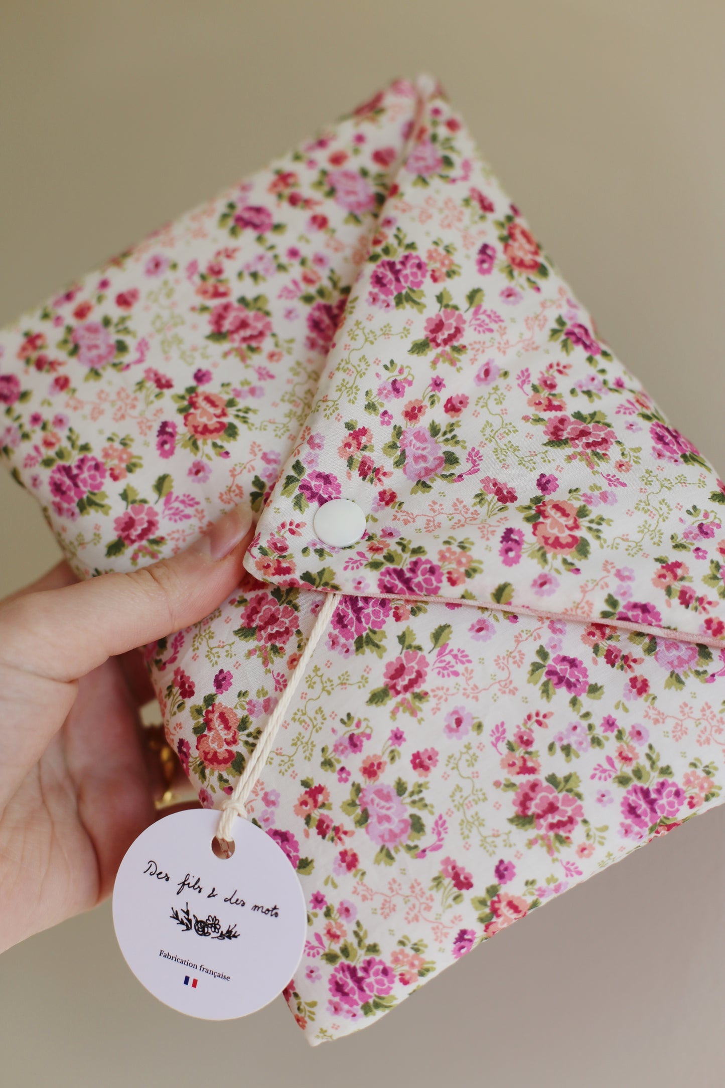 Housse pour livre de poche en Liberty of London fleuri rose, vue de face fermée, bouton pression blanc et étiquette ronde Des fils et des mots