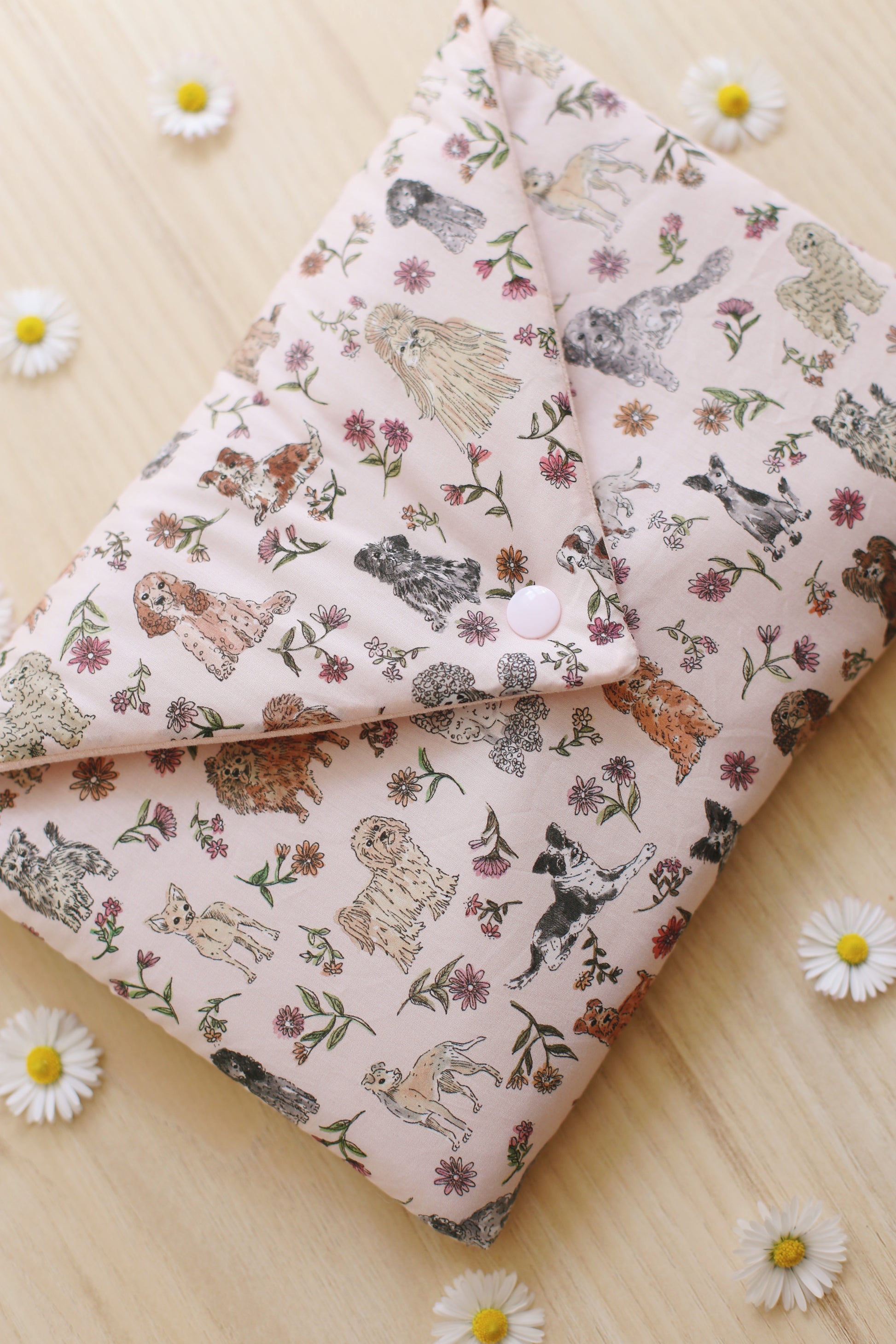 Housse pour liseuse en Liberty of London imprimé chiens et fleurs rose poudré, format liseuse 6 pouces, posée sur parquet bois entourée de marguerites