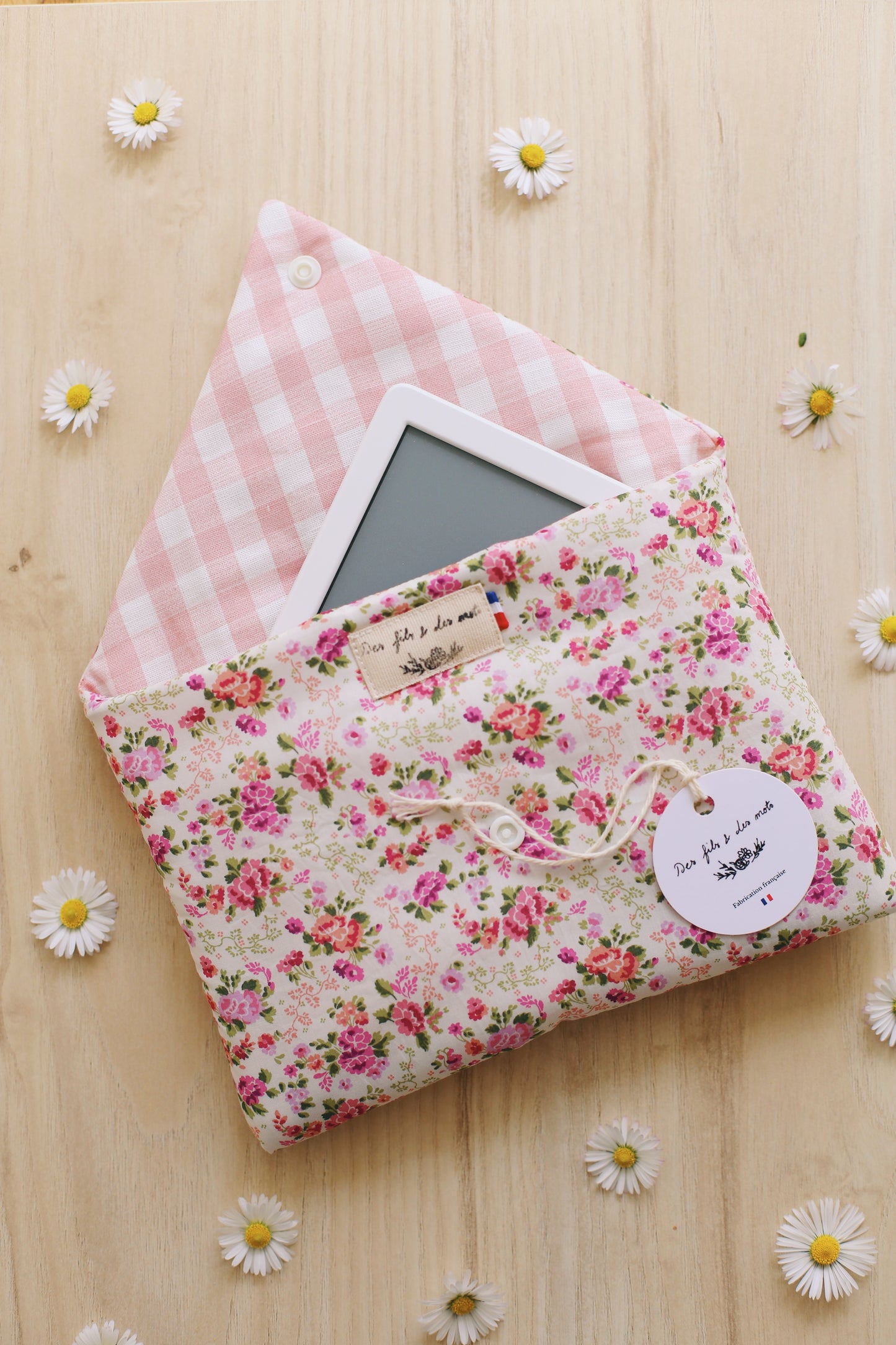 Housse pour liseuse Liberty of London fleuri rose ouverte, liseuse Kindle visible, doublure vichy rose, étiquette Des fils et des mots, bouton pression blanc, marguerites sur parquet bois